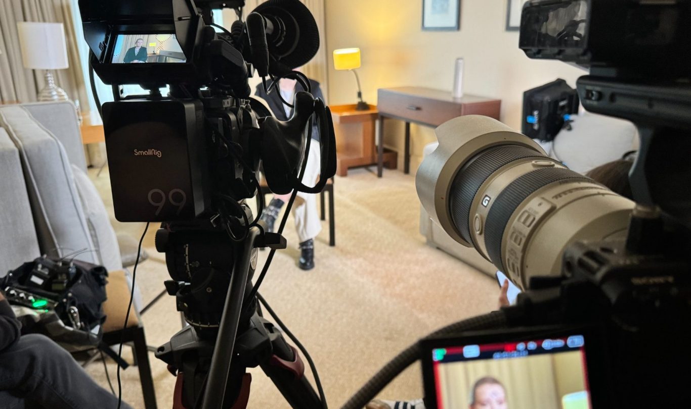 Interview-Szene mit Kameraequipment und einem sprechenden Interviewpartner im Hintergrund.